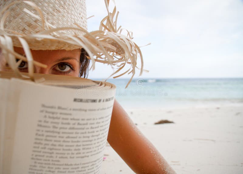 A mulher lê um livro na praia imagens de stock A mulher lê um livro na praia imagens de stock