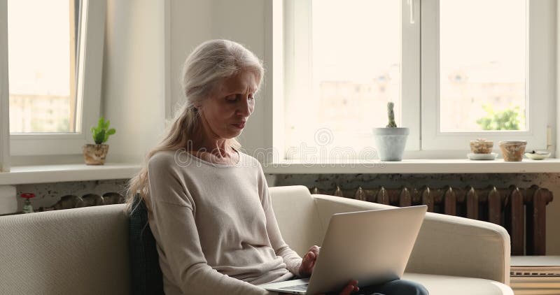 Mulher mais velha e carinhosa sentada no sofá, mandando mensagens no laptop