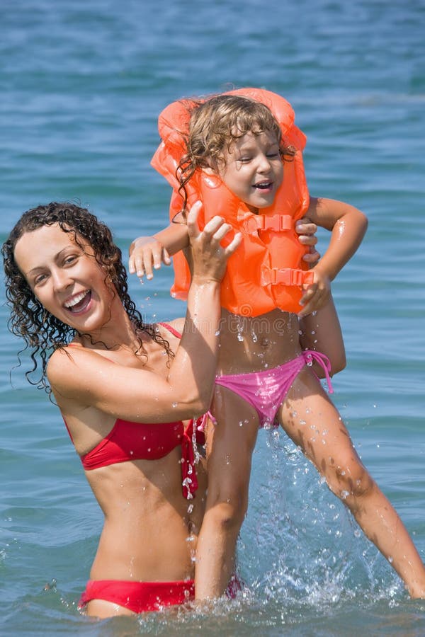 A mulher mantem-se na menina das mãos nos colete salva-vidas no mar foto de stock A mulher mantem-se na menina das mãos nos colete salva-vidas no mar foto de stock