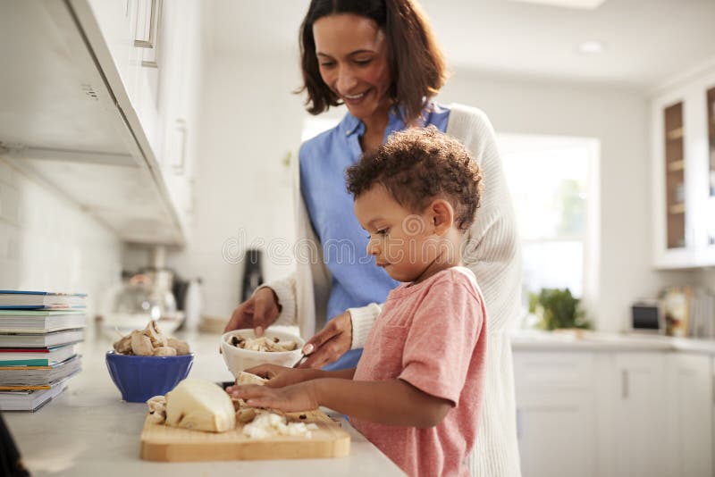 Mulher milenar e seu filho da criança que preparam o alimento que levanta-se junto em um worktop na cozinha, vista lateral, fim
