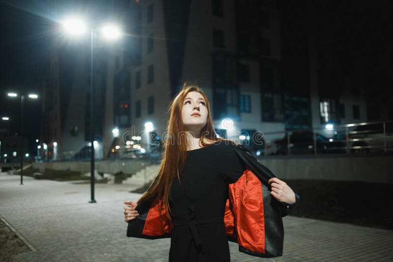 Mulher misteriosa do ruivo no revestimento e nos saltos altos elegantes do casaco de cabedal que anda na rua da cidade, atmosfera fotografia de stock royalty free Mulher misteriosa do ruivo no revestimento e nos saltos altos elegantes do casaco de cabedal que anda na rua da cidade, atmosfera fotografia de stock royalty free