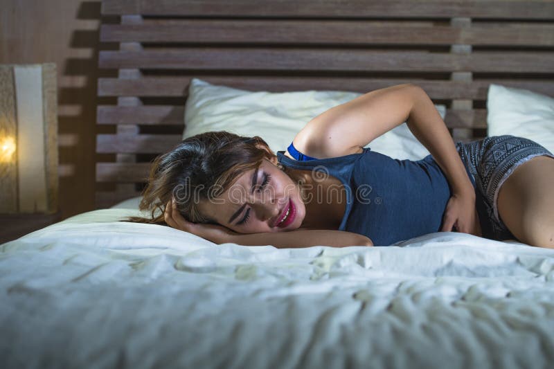 Mulher misturada latin asiática que encontra-se no ach de sofrimento do grampo de estômago da cama foto de stock Mulher misturada latin asiática que encontra-se no ach de sofrimento do grampo de estômago da cama foto de stock