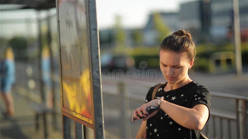 Mulher moreno que está na frente de um mapa na cidade, menina que olha a programação de ônibus e que olha o relógio