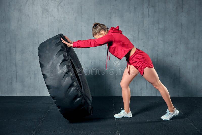 Mulher muscular nova que lança um pneu no treinamento duro com o instrutor pessoal no gym da garagem fotos de stock Mulher muscular nova que lança um pneu no treinamento duro com o instrutor pessoal no gym da garagem fotos de stock