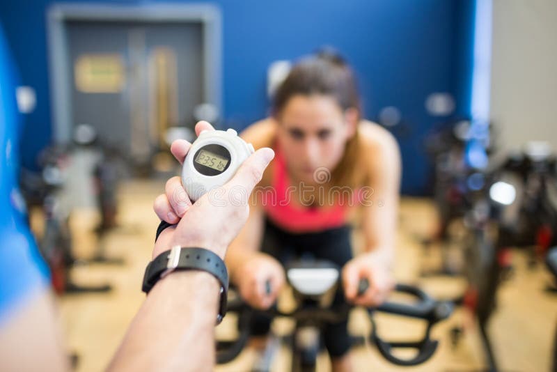 Mulher na bicicleta de exercício com o instrutor que cronometra a fotos de stock Mulher na bicicleta de exercício com o instrutor que cronometra a fotos de stock