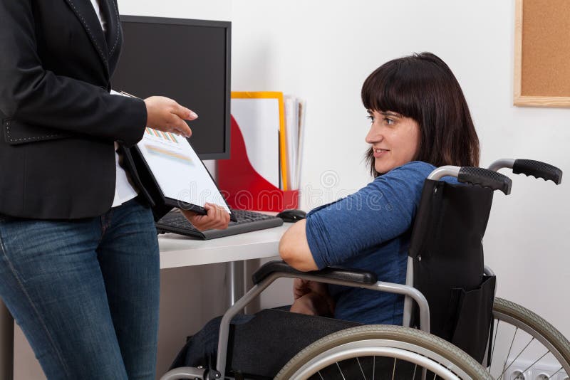 Young women on wheelchair analyzing charts with her boss. Young women on wheelchair analyzing charts with her boss