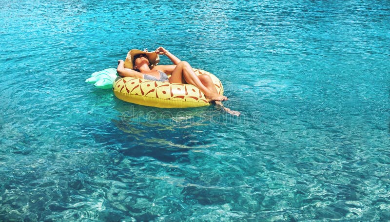 A mulher nada na água do mar inflável do anel do abacaxi na claro fotografia de stock A mulher nada na água do mar inflável do anel do abacaxi na claro fotografia de stock