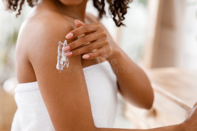 Mulher negra a aplicar loção de corpo humedecedor na pele após o chuveiro