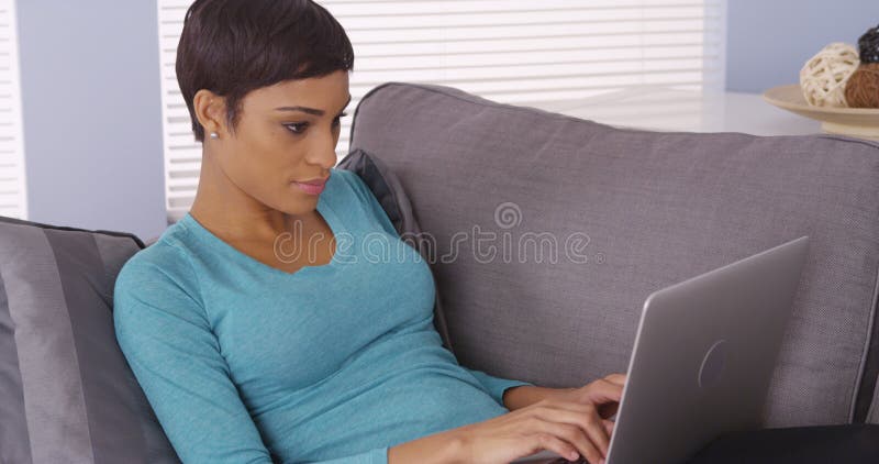 Mulher negra atrativa que usa o portátil no sofá imagem de stock Mulher negra atrativa que usa o portátil no sofá imagem de stock