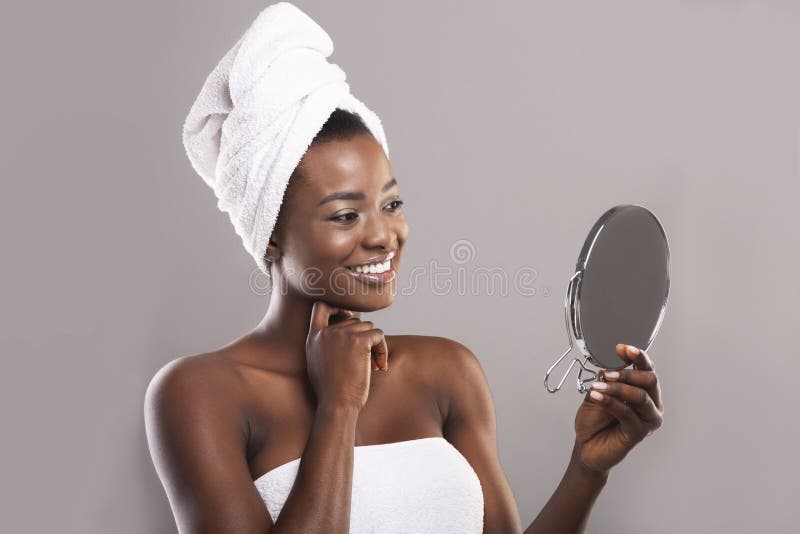 Mulher negra atrativa segurando um espelho e olhando sua pele perfeita