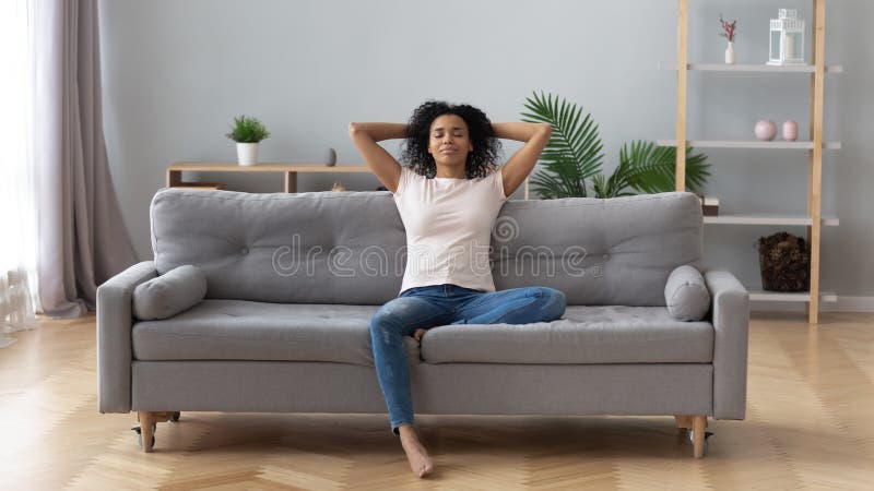 Mulher negra da calma que relaxa no sofá confortável na sala de visitas