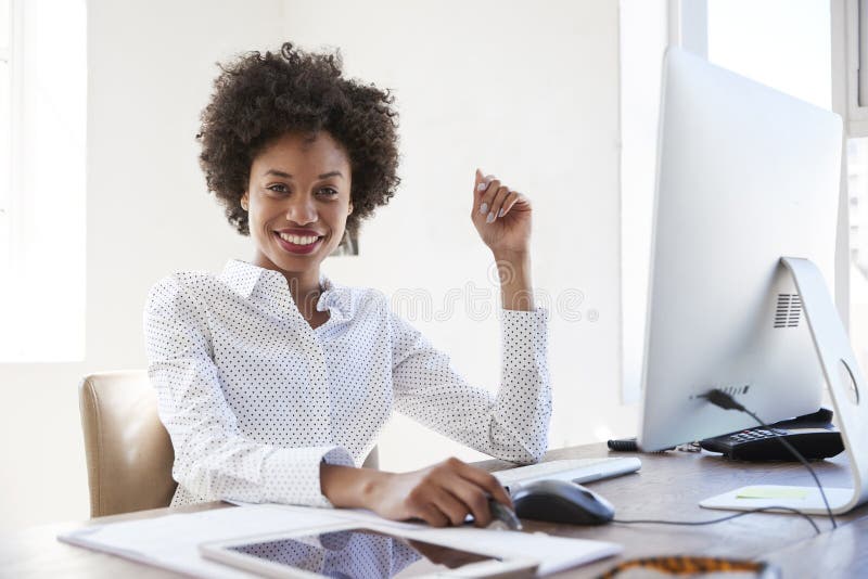 Mulher negra nova em um escritório que sorri à câmera, fim acima