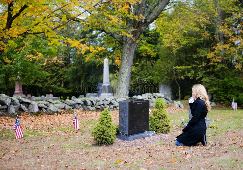 A side view of a young woman kneeling in a cemetery. A side view of a young woman kneeling in a cemetery.