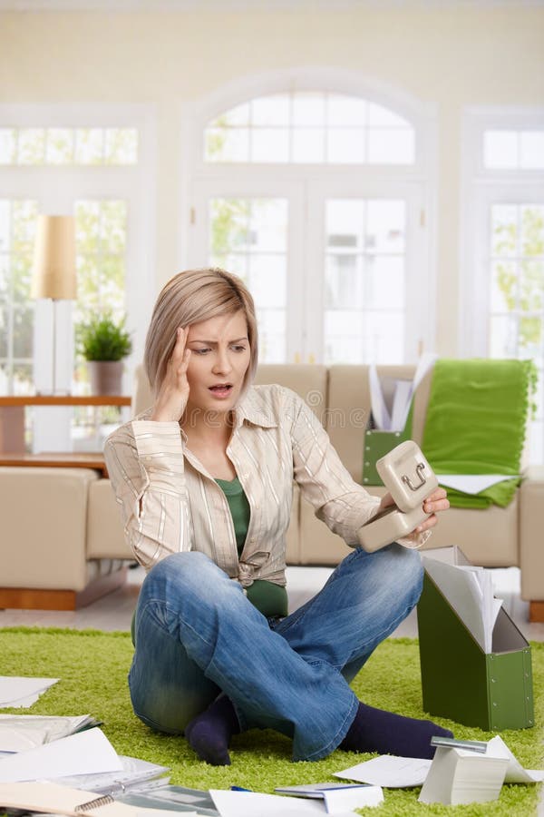 Shocked woman sitting at home surrounded with documents, looking at money box unbelieving. Shocked woman sitting at home surrounded with documents, looking at money box unbelieving.