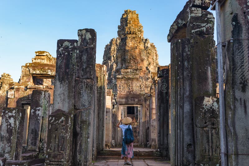 Mulher no templo de Bayon que olha as caras de pedra, Angkor Thom, céu azul claro da luz da manhã Conceito da meditação do budism fotografia de stock Mulher no templo de Bayon que olha as caras de pedra, Angkor Thom, céu azul claro da luz da manhã Conceito da meditação do budism fotografia de stock