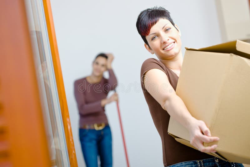 Woman lifting cardboard box while moving home, smiling. Woman lifting cardboard box while moving home, smiling.