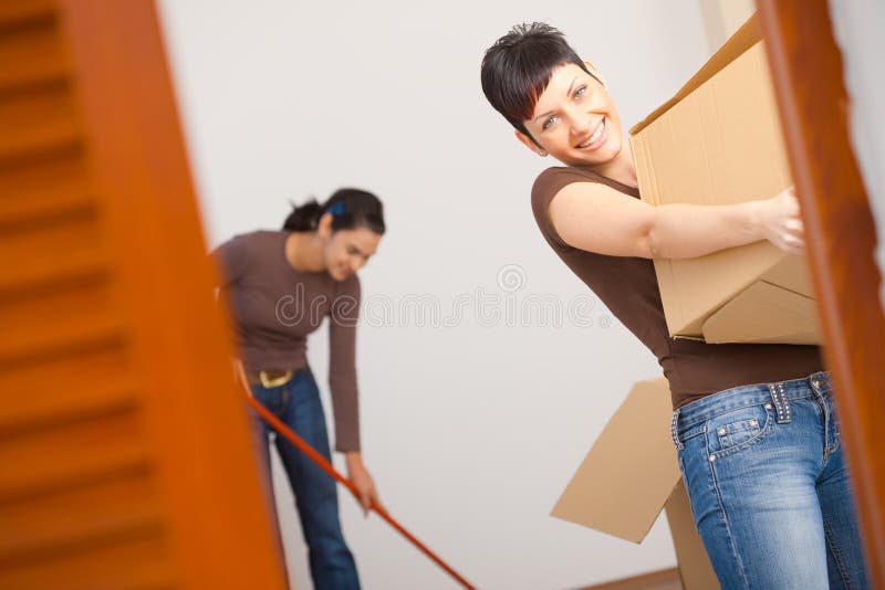 Woman lifting cardboard box while moving home, smiling. Woman lifting cardboard box while moving home, smiling.