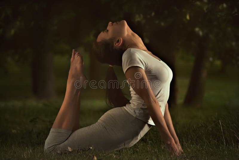A mulher nova da ioga da aptidão que faz o esticão exercita na grama fotos de stock royalty free A mulher nova da ioga da aptidão que faz o esticão exercita na grama fotos de stock royalty free