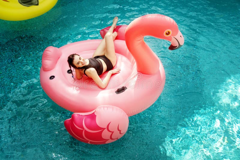 Mulher nova e 'sexy', tendo o divertimento e rindo em um flamingo cor-de-rosa gigante inflável no colchão de ar do flutuador da a fotografia de stock Mulher nova e 'sexy', tendo o divertimento e rindo em um flamingo cor-de-rosa gigante inflável no colchão de ar do flutuador da a fotografia de stock