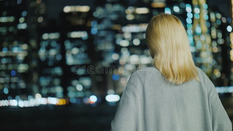 A mulher olha as luzes da metrópole da noite, vista traseira imagens de stock royalty free A mulher olha as luzes da metrópole da noite, vista traseira imagens de stock royalty free