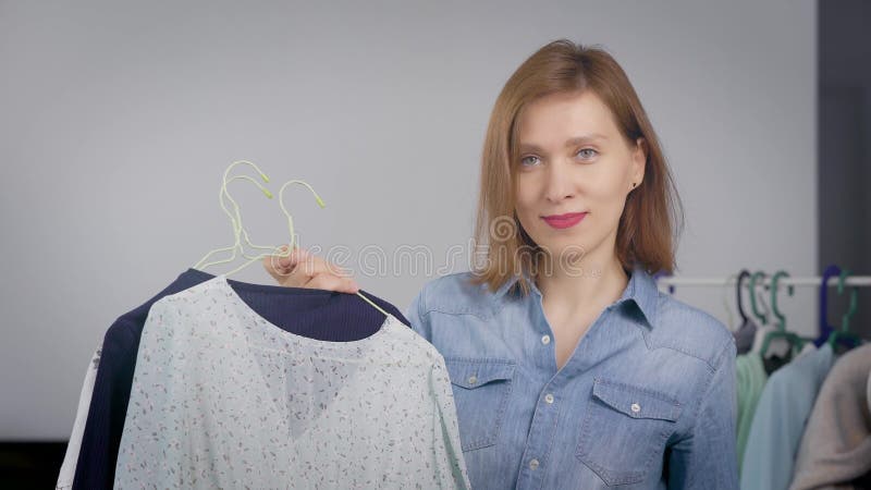 A mulher pessoal do estilista está olhando a câmera e está sorrindo, está guardando ganchos com roupa e está mostrando-a