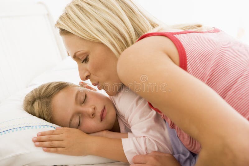 Mulher a acordar uma menina na cama com um beijo imagem de stock