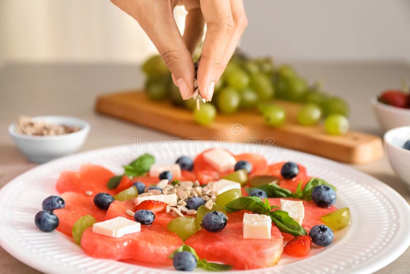Mulher que adiciona sementes de girassol à salada doce com melancia e feta na placa, close up imagens de stock royalty free Mulher que adiciona sementes de girassol à salada doce com melancia e feta na placa, close up imagens de stock royalty free