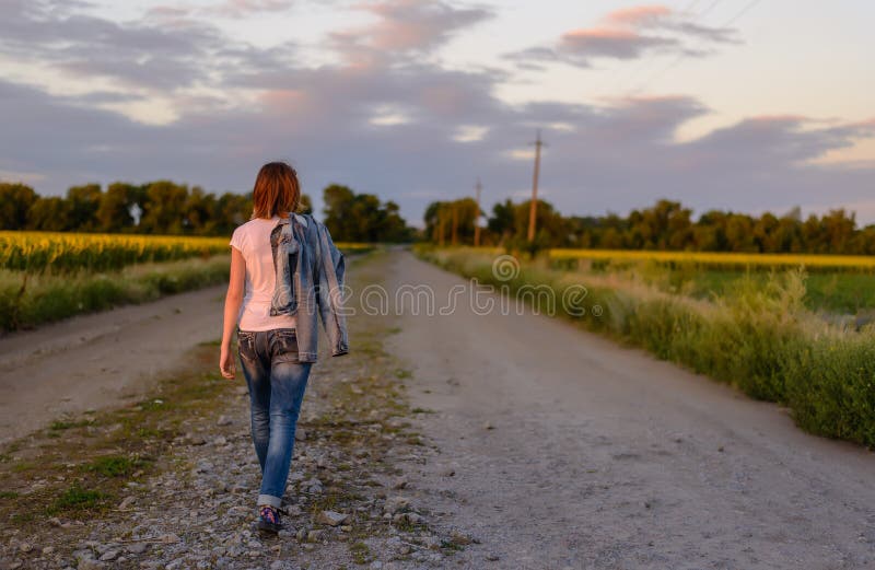Mulher que anda abaixo de uma estrada secundária foto de stock Mulher que anda abaixo de uma estrada secundária foto de stock