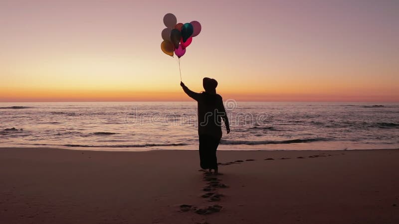 Mulher que anda na praia com balões