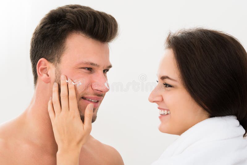 Mulher que aplica o creme hidratante no mordente do homem imagem de stock Mulher que aplica o creme hidratante no mordente do homem imagem de stock