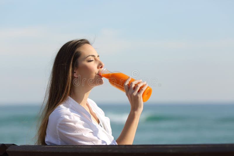 Mulher que bebe um suco de laranja na praia foto de stock Mulher que bebe um suco de laranja na praia foto de stock