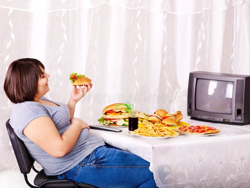 Mulher que come a tevê do fast food e da observação. imagem de stock royalty free Mulher que come a tevê do fast food e da observação. imagem de stock royalty free
