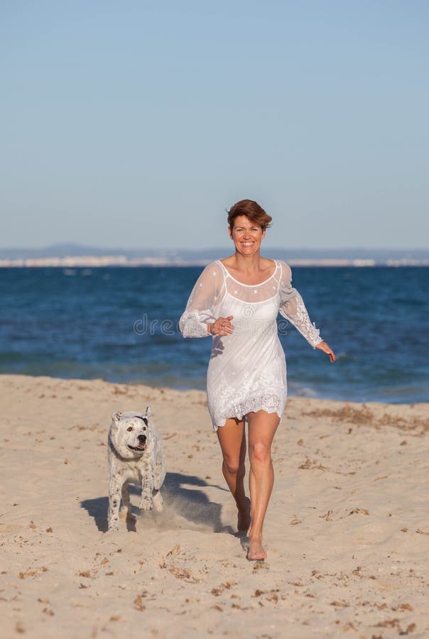 Mulher que corre na praia com cão de estimação foto de stock royalty free Mulher que corre na praia com cão de estimação foto de stock royalty free