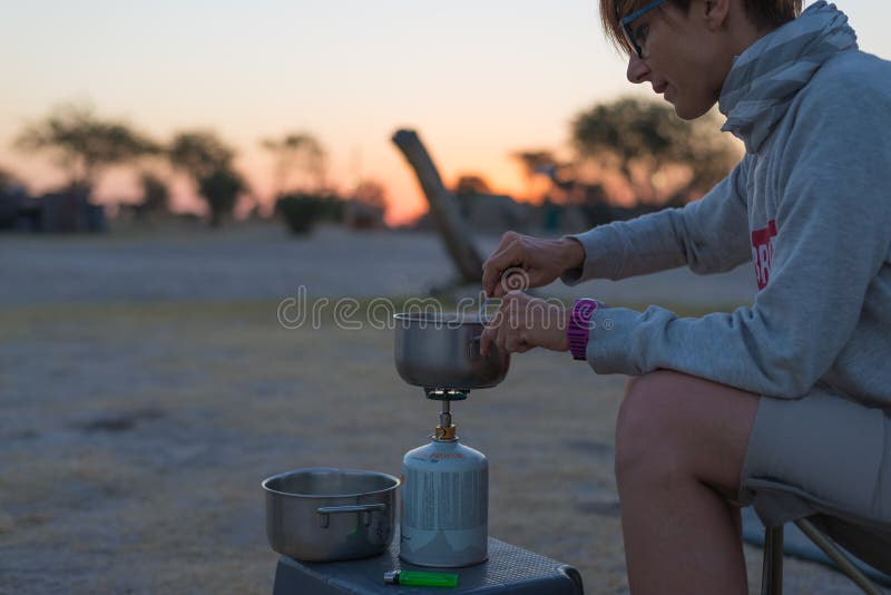 Mulher que cozinha com o fogão de gás no local de acampamento no crepúsculo Queimador, potenciômetro e fumo de gás da água a ferv fotografia de stock royalty free Mulher que cozinha com o fogão de gás no local de acampamento no crepúsculo Queimador, potenciômetro e fumo de gás da água a ferv fotografia de stock royalty free