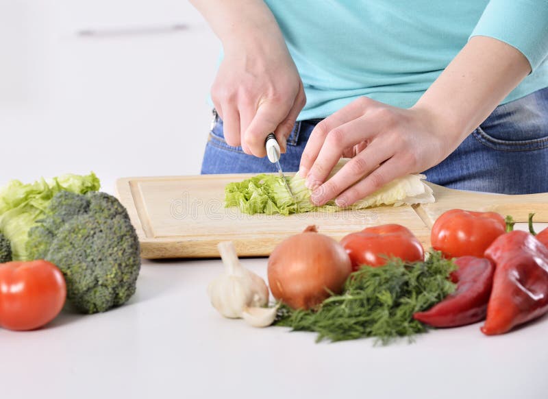 Mulher que cozinha na cozinha nova que faz o alimento saudável com vegetais