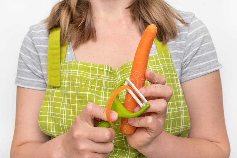 Mulher que descasca uma cenoura usando o descascador do alimento fotografia de stock Mulher que descasca uma cenoura usando o descascador do alimento fotografia de stock