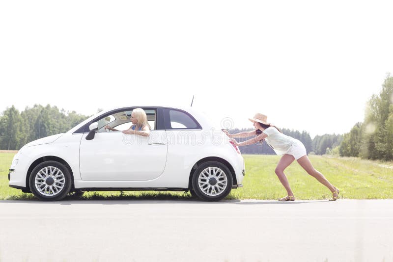 Mulher que empurra o carro dividido na estrada secundária imagem de stock Mulher que empurra o carro dividido na estrada secundária imagem de stock