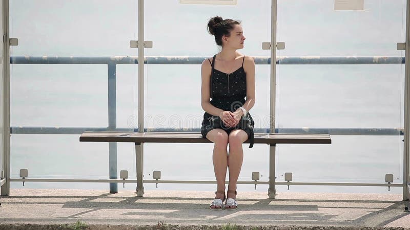 A mulher que espera um ônibus na parada do ônibus olha ao redor e falta