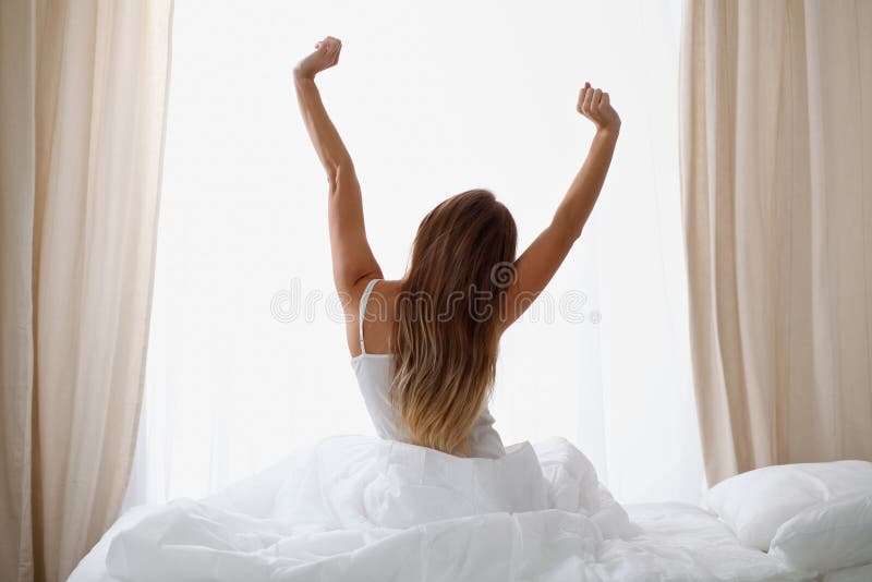A mulher que estica na cama após acorda, vista traseira, incorporando um dia feliz e relaxado após a boa noite de sono Sonhos doc