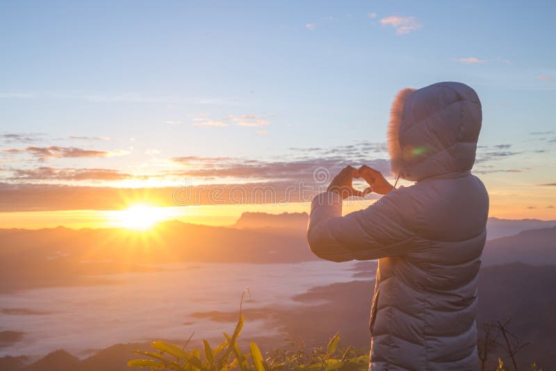 A mulher que faz a forma do coração durante a elevação do sol, deus é conceito do amor, forma do coração, turismo da montanha, sí foto de stock A mulher que faz a forma do coração durante a elevação do sol, deus é conceito do amor, forma do coração, turismo da montanha, sí foto de stock