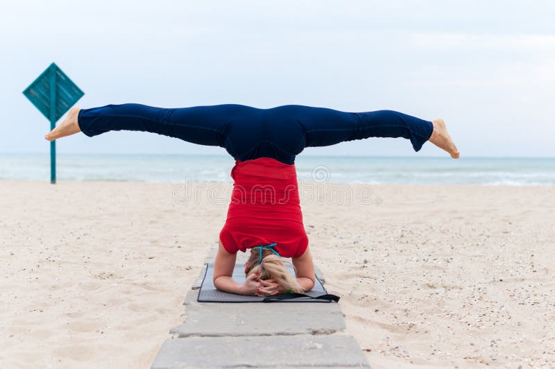 Mulher que faz o shirshasana do konasana do upavishtha do asana da ioga, pose encadernada do ângulo no suporte principal no fundo imagem de stock Mulher que faz o shirshasana do konasana do upavishtha do asana da ioga, pose encadernada do ângulo no suporte principal no fundo imagem de stock