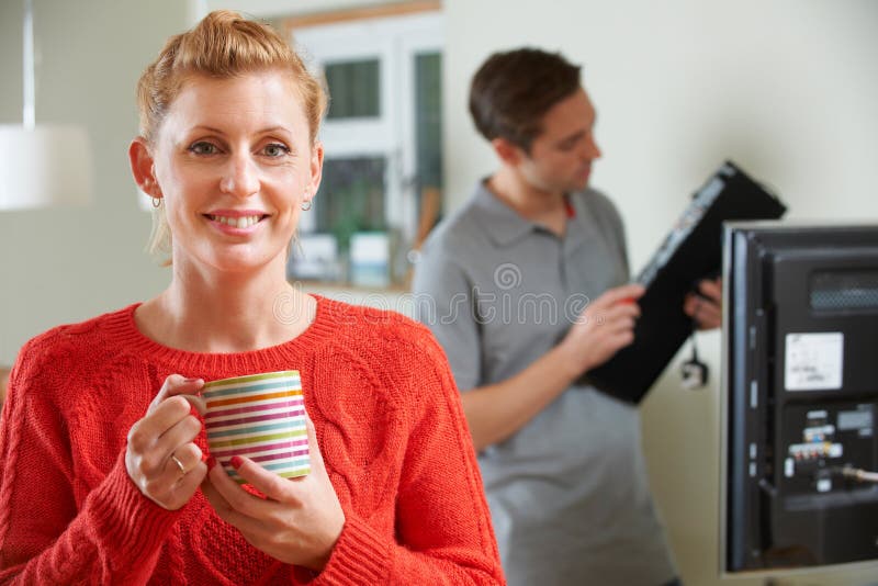 Mulher que guarda a caneca enquanto equipamento da tevê de Installs do coordenador foto de stock royalty free Mulher que guarda a caneca enquanto equipamento da tevê de Installs do coordenador foto de stock royalty free