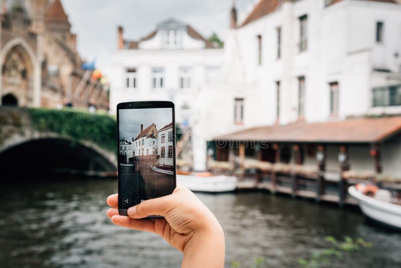 Mulher que guarda um telefone que toma uma foto à arquitetura da cidade de Bruges foto de stock Mulher que guarda um telefone que toma uma foto à arquitetura da cidade de Bruges foto de stock
