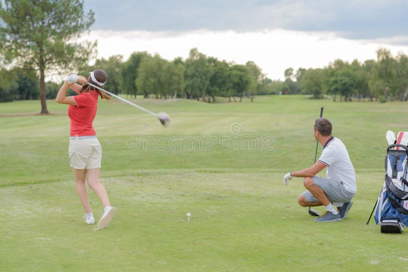 Mulher que joga o tiro de observação do marido do golfe fotografia de stock royalty free Mulher que joga o tiro de observação do marido do golfe fotografia de stock royalty free