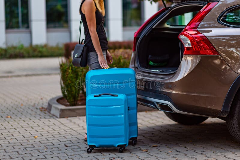 Mulher que põe duas malas de viagem plásticas azuis ao tronco de carro fotos de stock Mulher que põe duas malas de viagem plásticas azuis ao tronco de carro fotos de stock