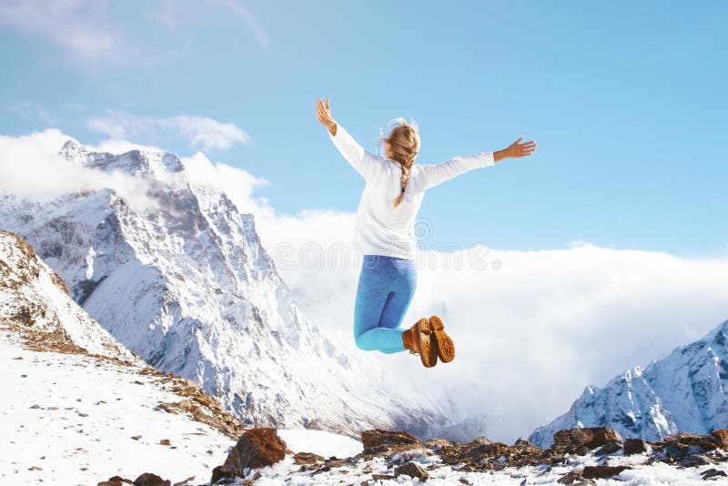 Unrecognizable young woman jumping on top of the mountain over blue skies, freedom and joy, winter season with snow. Unrecognizable young woman jumping on top of the mountain over blue skies, freedom and joy, winter season with snow