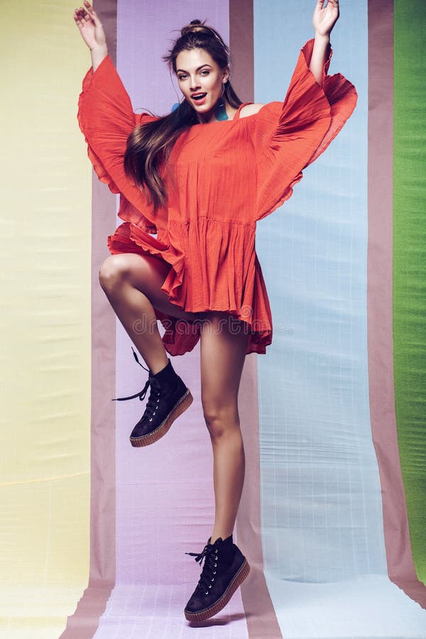 A mulher que salta no vestido alaranjado de fluxo no multi fundo foto de stock A mulher que salta no vestido alaranjado de fluxo no multi fundo foto de stock