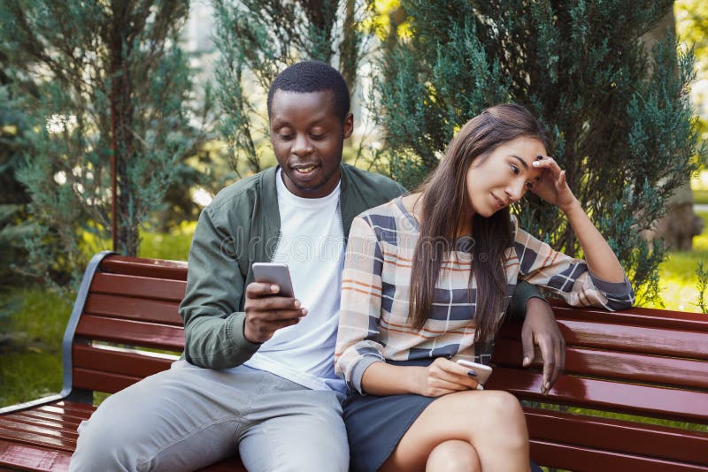 Mulher que senta-se no parque com o homem que usa o smartphone foto de stock Mulher que senta-se no parque com o homem que usa o smartphone foto de stock