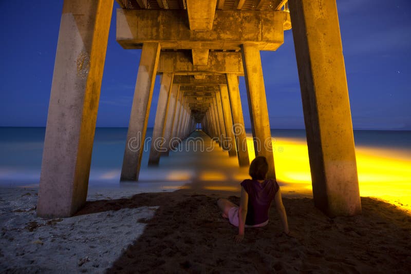Mulher que senta-se sob o passeio à beira mar na noite fotografia de stock royalty free Mulher que senta-se sob o passeio à beira mar na noite fotografia de stock royalty free