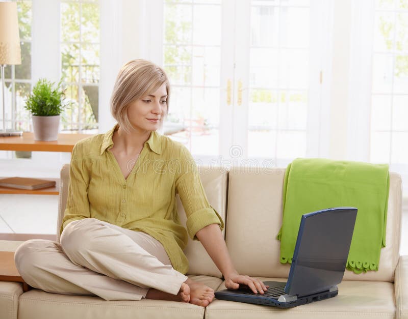 Mulher que usa o computador no sofá imagem de stock Mulher que usa o computador no sofá imagem de stock